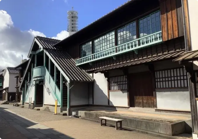 A two-story reconstructed historical building in Dejima, with exterior stairs and a balcony featuring teal-colored railings.