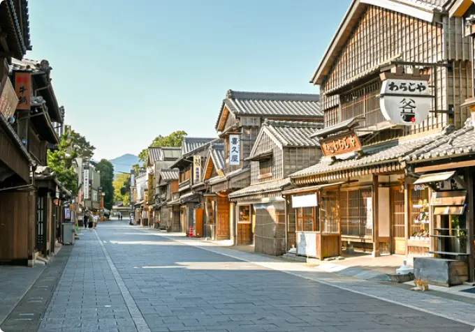 A view down a stone-paved street lined with traditional dark wooden buildings, resembling a historic temple town like present-day Okage Yokocho near Ise-jingu Shrine.