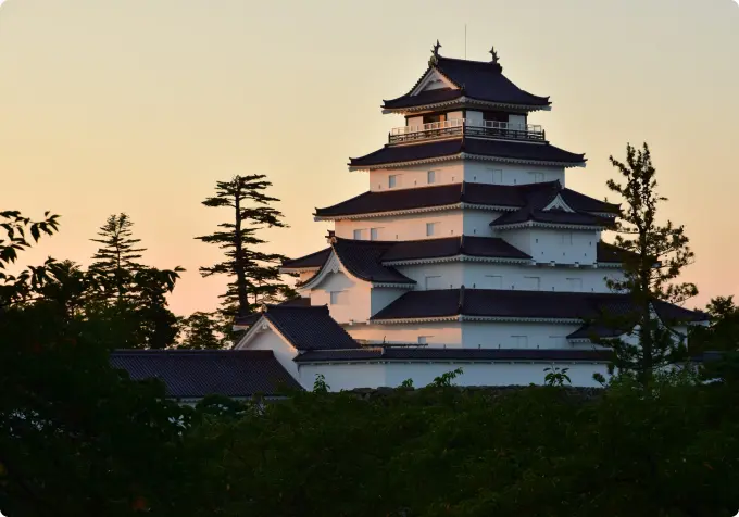 Tsuruga Castle keep at dusk, with the white walls and dark roof contrasting against the yellow-orange sky.