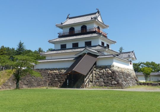 Shiroishi Castle main keep and stone foundation under a clear sky.