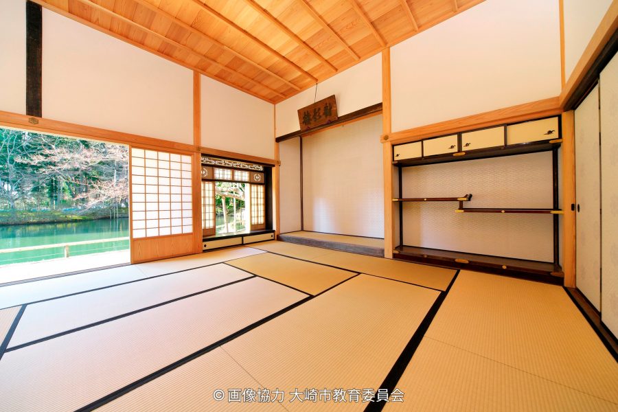 Interior of a traditional Japanese room with tatami mats, wooden ceiling, and sliding doors opening to a pond view.