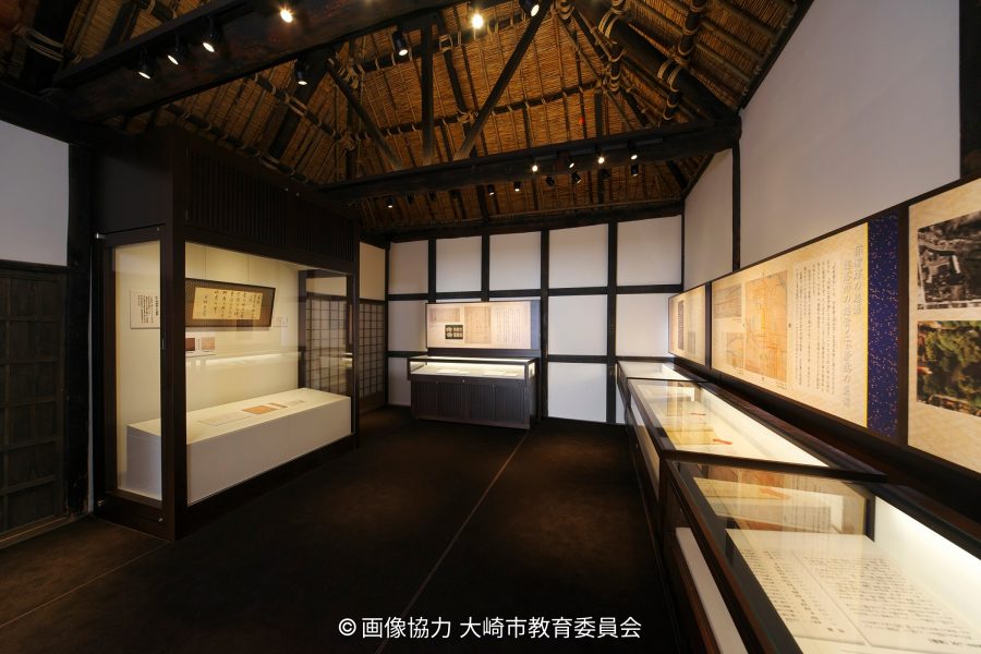 Exhibition room interior with a high thatched roof, displaying historical documents and artifacts in glass cases.