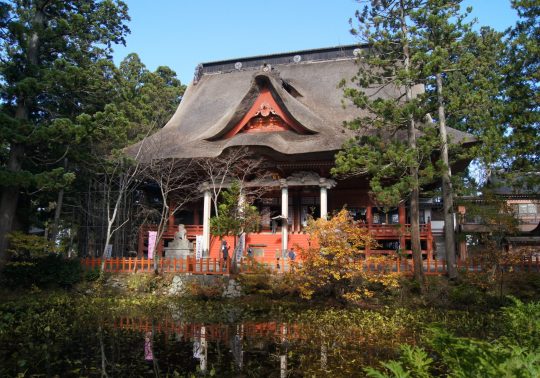 The Sanjin Gosai-den main shrine on Mt. Haguro with its large thatched roof, seen across a reflective pond.