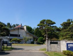 The entrance gate and modern museum building of the Homma Museum of Art on a sunny day.