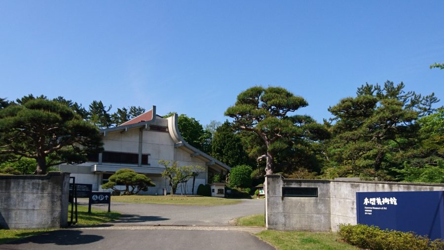 The entrance gate and modern museum building of the Homma Museum of Art on a sunny day.