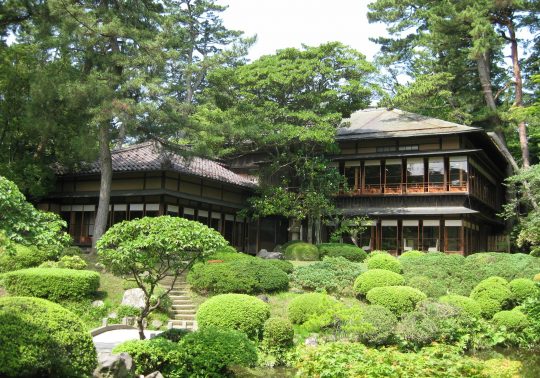 A traditional two-story Seienkaku villa with a tiled roof, surrounded by a lush Japanese garden.