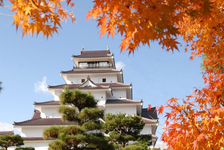 Tsuruga Castle keep framed by vibrant red and orange autumn maple leaves.