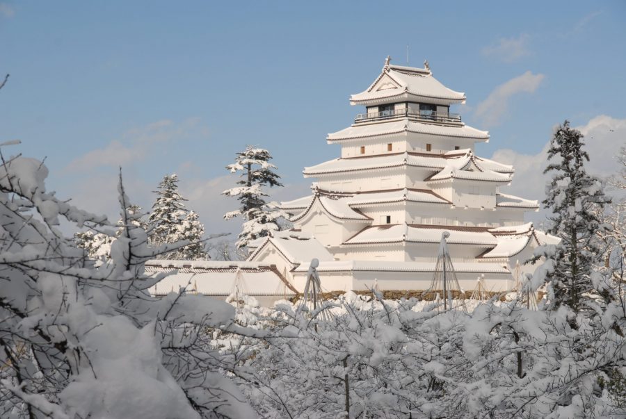 Tsuruga Castle keep covered in snow, seen through snowy tree branches in winter.