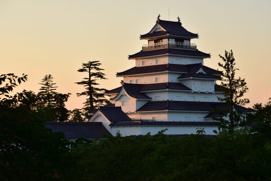 Tsuruga Castle keep at dusk, with the white walls and dark roof contrasting against the yellow-orange sky.