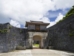 The Kankaimon Gate of Shuri Castle, an arched stone gate flanked by high stone walls with two stone Shisa statues on pedestals.