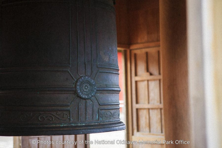 A close-up of a large, dark bronze temple bell with intricate circular patterns, hanging within a wooden structure.
