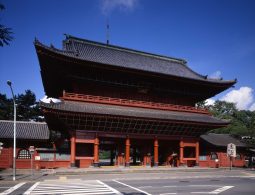 The towering red and black Sangedatsu-mon Gate (Main Gate) of Zojo-ji Temple, standing over a busy city street intersection.