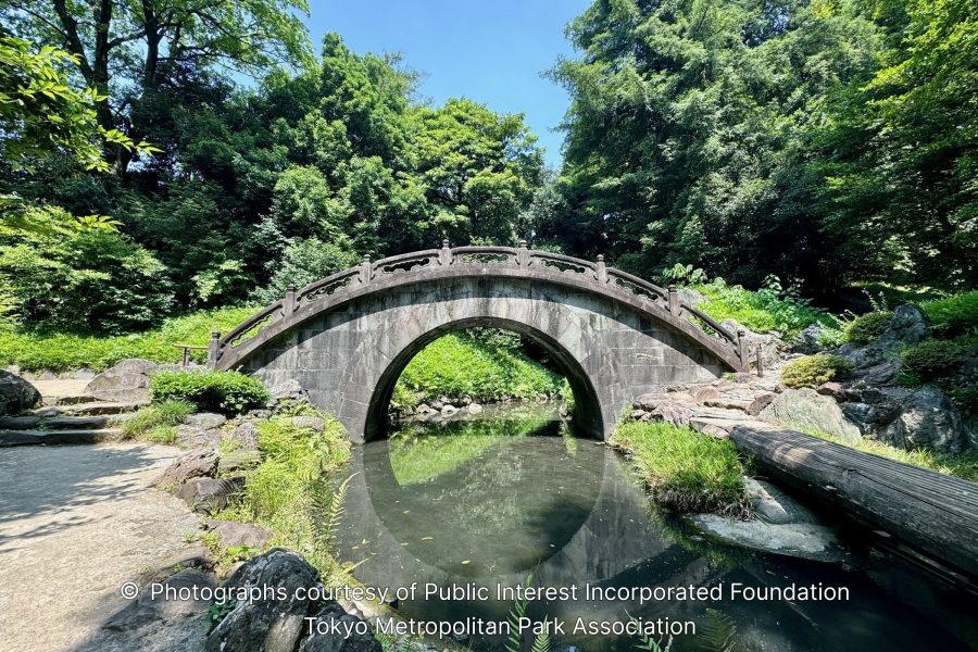 The Engetsukyō (Full Moon Bridge), a traditional stone arch bridge crossing a small, calm stream in a lush, tree-filled landscape.