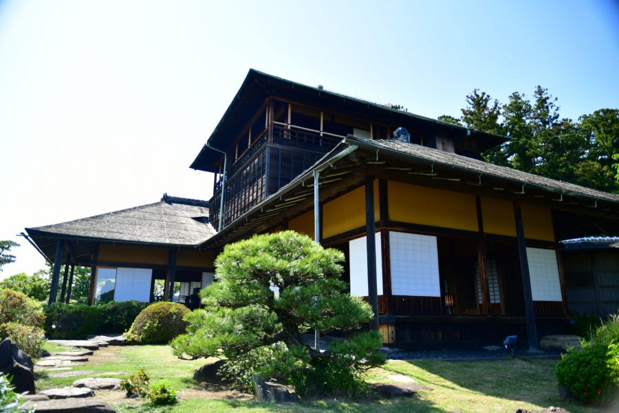 Close-up, low-angle view of the traditional, two-story Kobuntei building and a large sculpted pine tree.