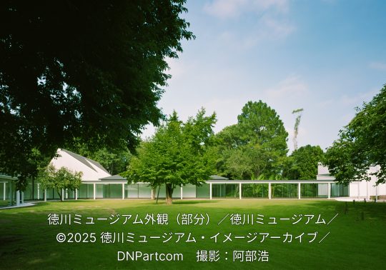 Exterior of the modern Tokugawa Museum in Mito, featuring a sleek white building with large glass windows connected by a covered walkway, surrounded by a lush green lawn and trees.