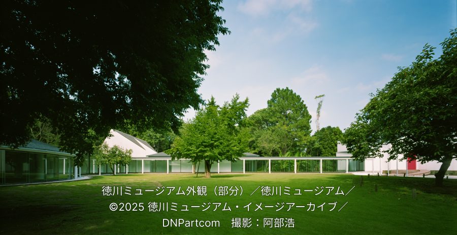 Exterior of the modern Tokugawa Museum in Mito, featuring a sleek white building with large glass windows connected by a covered walkway, surrounded by a lush green lawn and trees.