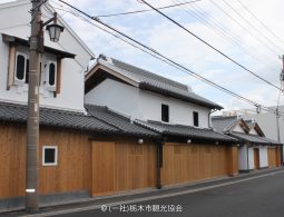 Traditional Japanese storehouse-style buildings with white walls, tiled roofs, and new wooden fences along the street.