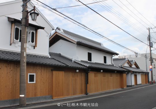 Traditional Japanese storehouse-style buildings with white walls, tiled roofs, and new wooden fences along the street.