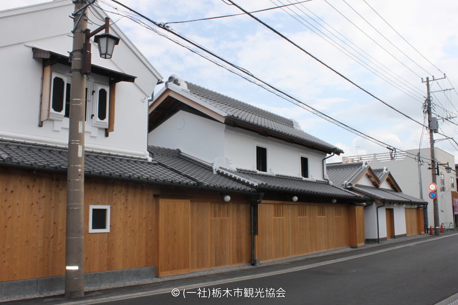 Traditional Japanese storehouse-style buildings with white walls, tiled roofs, and new wooden fences along the street.