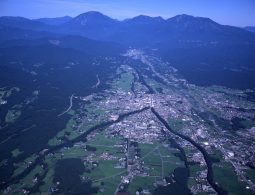An aerial view of a city (likely Nikko or the surrounding area) nestled in a valley, surrounded by green mountains and fields.