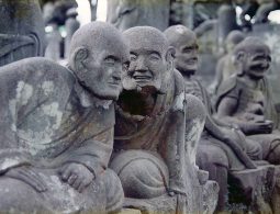 Close-up of several weathered, smiling, or expressive stone Rakan (Arhat) statues in the Gohyaku Rakan area.