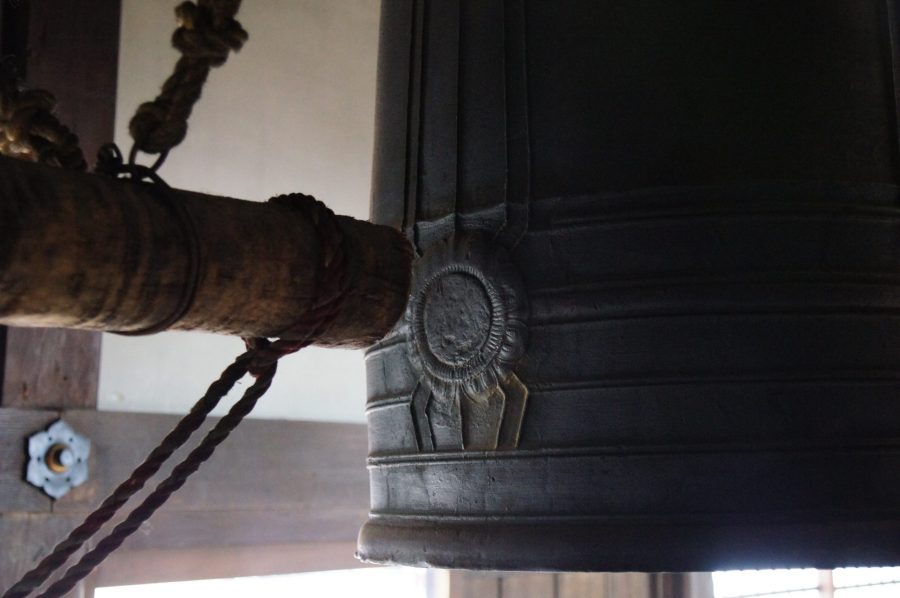 Close-up of a large, dark temple bell and the wooden striking beam in the belfry of Kita-in Temple.