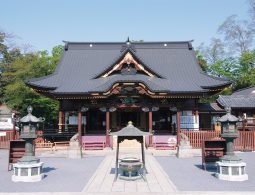 The main hall of a temple with a dark tiled roof, elevated stone base, and a large metal incense burner in the courtyard.