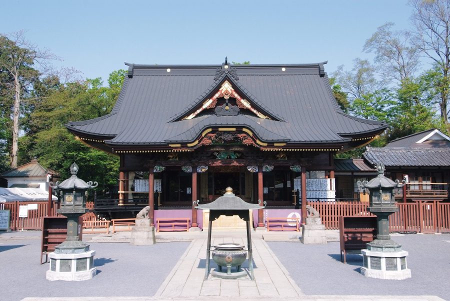 The main hall of a temple with a dark tiled roof, elevated stone base, and a large metal incense burner in the courtyard.
