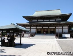 The modern Great Main Hall (Dai Hondo) of Naritasan Shinsho-ji Temple under a bright blue sky.