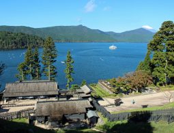 Overhead view of the reconstructed Hakone Checkpoint on the shore of Lake Ashi, with Mount Fuji visible in the background.