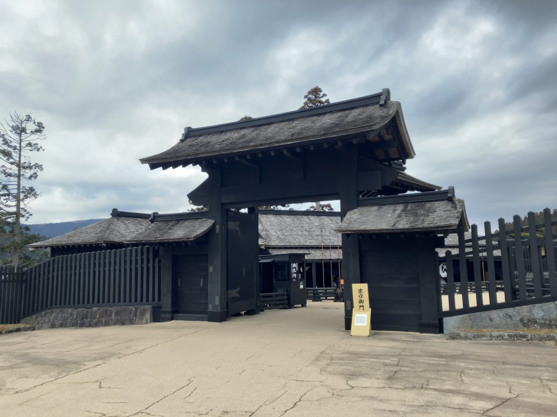 The reconstructed main gate of the Hakone Checkpoint with dark wood and a tiled roof, under an overcast sky.