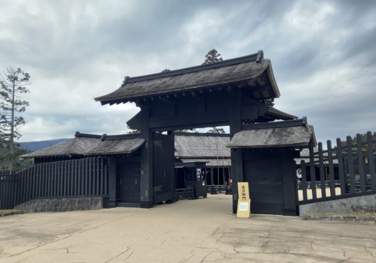 The reconstructed main gate of the Hakone Checkpoint with dark wood and a tiled roof, under an overcast sky.