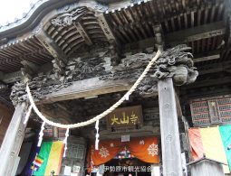 The richly carved wooden entrance gate of Oyama-dera Temple, with ropes and colorful flags.