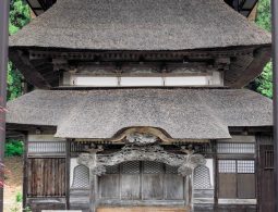 A traditional Japanese temple building entrance with a thick, thatched roof and complex wooden carvings over the doorway.
