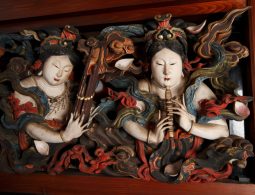 A close-up of a richly painted and carved wooden panel depicting two female figures in elaborate robes, possibly celestial maidens (tennyo).