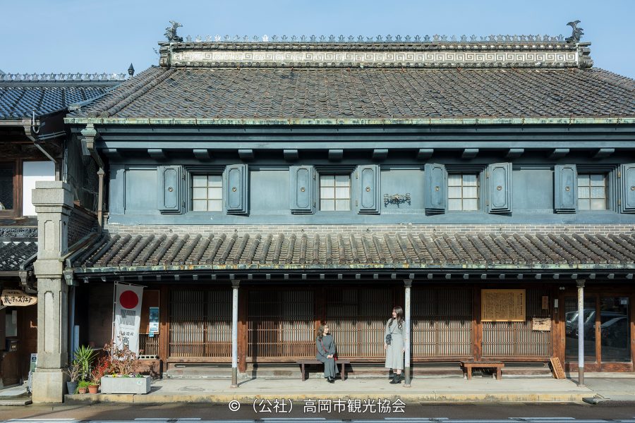A perfectly preserved traditional merchant house with a tiled roof, blue facade, and latticework windows on the Yamacho-suji street.