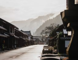 A view down the street of Kumagawa-juku in the early morning, with traditional houses on both sides and foggy, tree-covered mountains in the distance.