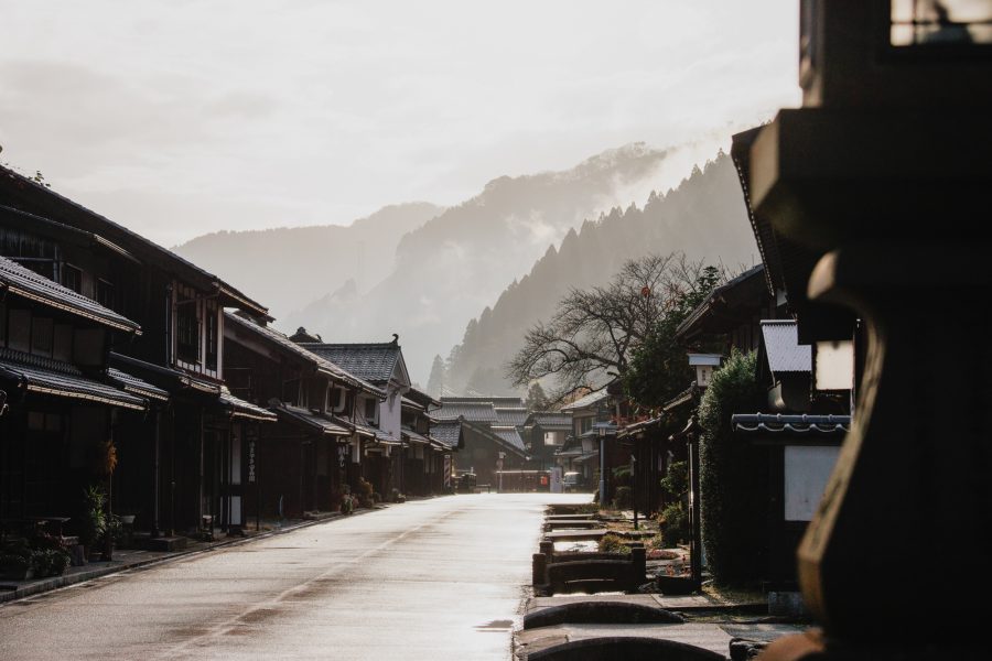 A view down the street of Kumagawa-juku in the early morning, with traditional houses on both sides and foggy, tree-covered mountains in the distance.