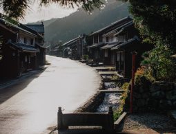 An atmospheric view of the Kumagawa-juku street and a stone-lined channel of running water, captured in soft morning light.