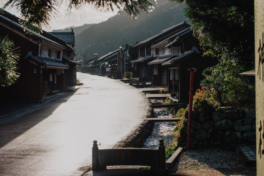 An atmospheric view of the Kumagawa-juku street and a stone-lined channel of running water, captured in soft morning light.