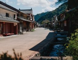 The preserved main street of Kumagawa-juku post town, lined with traditional wooden machiya houses, leading toward forested hills.