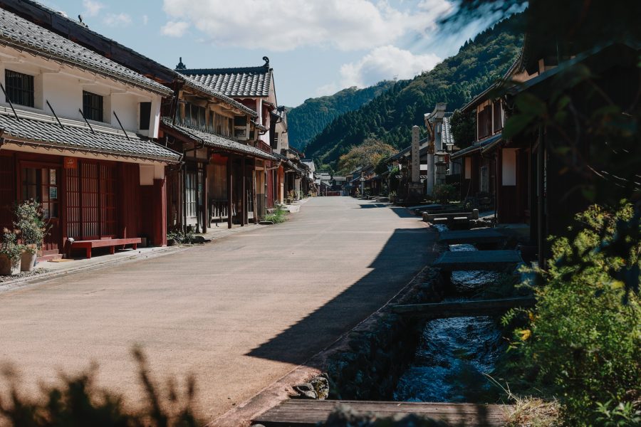 The preserved main street of Kumagawa-juku post town, lined with traditional wooden machiya houses, leading toward forested hills.