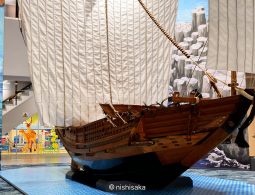 A large, detailed wooden model of a historic Japanese trade ship (Higaki Kaisen or similar) on display indoors, with white sails raised.