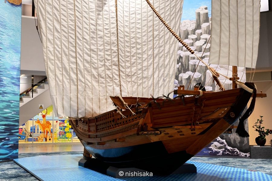 A large, detailed wooden model of a historic Japanese trade ship (Higaki Kaisen or similar) on display indoors, with white sails raised.