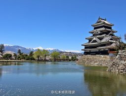 Side view of the black and white castle keep, with the snow-capped Japanese Alps visible in the background over the moat.