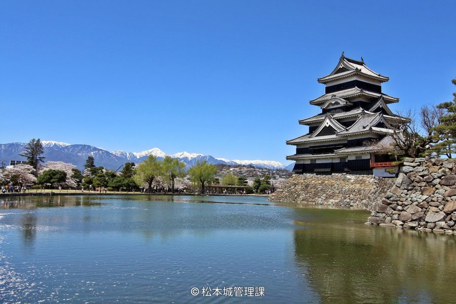 Side view of the black and white castle keep, with the snow-capped Japanese Alps visible in the background over the moat.