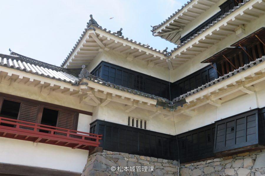 Close-up of the upper white plaster and black wooden section of the castle, showing the eaves and tiled roofs.