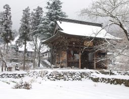 A traditional Japanese temple building covered in snow, surrounded by trees and a snow-covered landscape on a winter day.