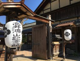 The wooden entrance gate to the Hokusai Museum (Hokusai-kan) in Obuse, flanked by two large white Japanese paper lanterns with black calligraphy.