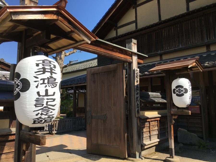 The wooden entrance gate to the Hokusai Museum (Hokusai-kan) in Obuse, flanked by two large white Japanese paper lanterns with black calligraphy.